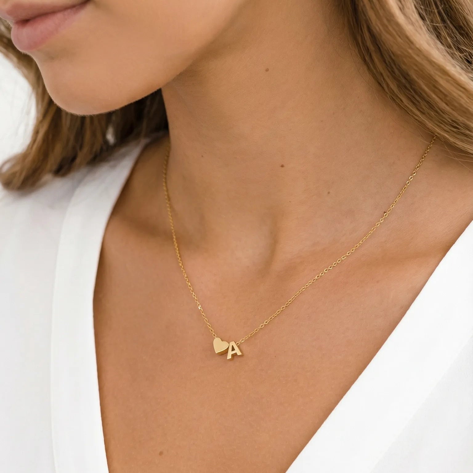 Gold necklace with a small pendant worn by a person in a white top.