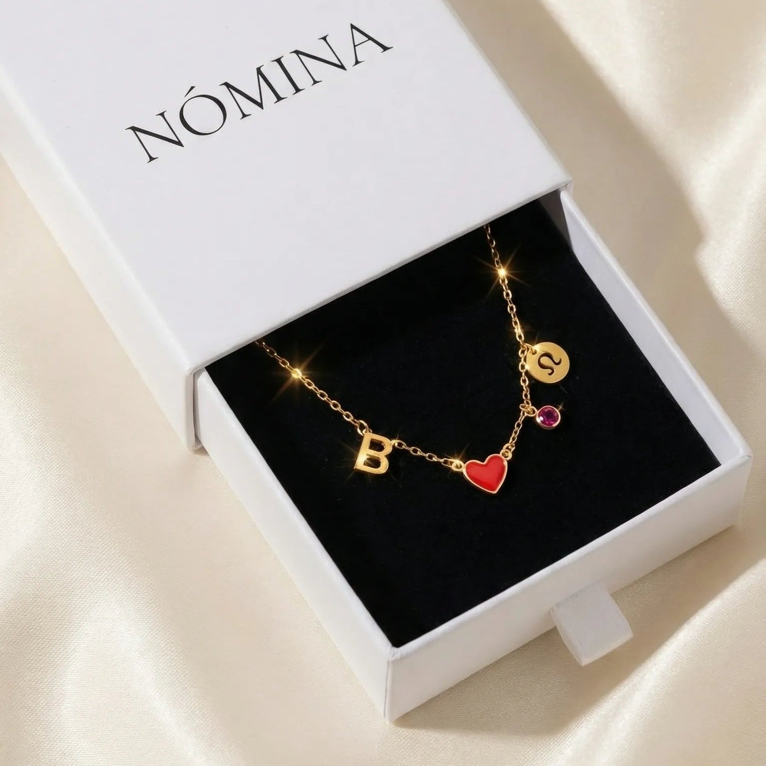 Gold necklace with heart and circle pendants in a Nomina box on a beige fabric background