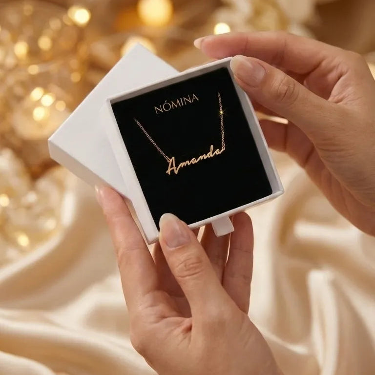 Person holding a necklace with 'Amanda' engraved, displayed on a white box against a warm, blurred background.