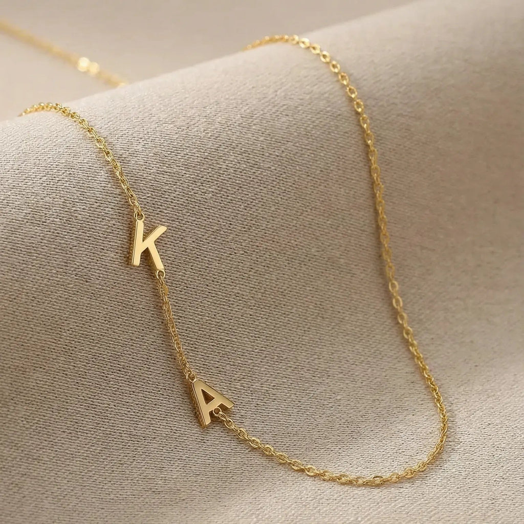 Gold necklace with 'K' pendant on a beige surface