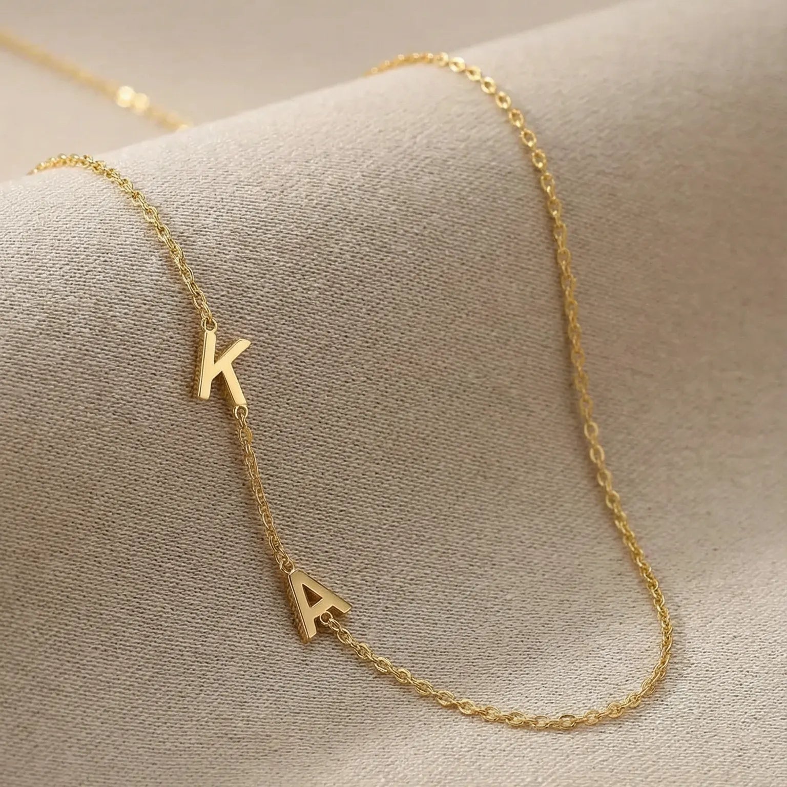 Gold necklace with 'K' pendant on a beige surface